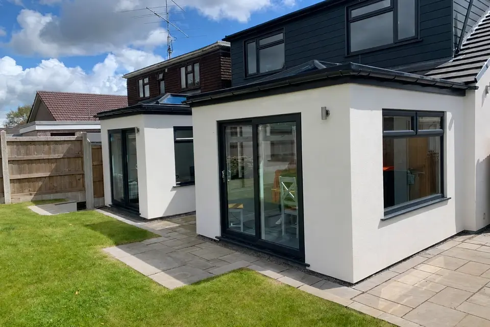 Modern white modular home extension with dark-framed glazing beside a lawn