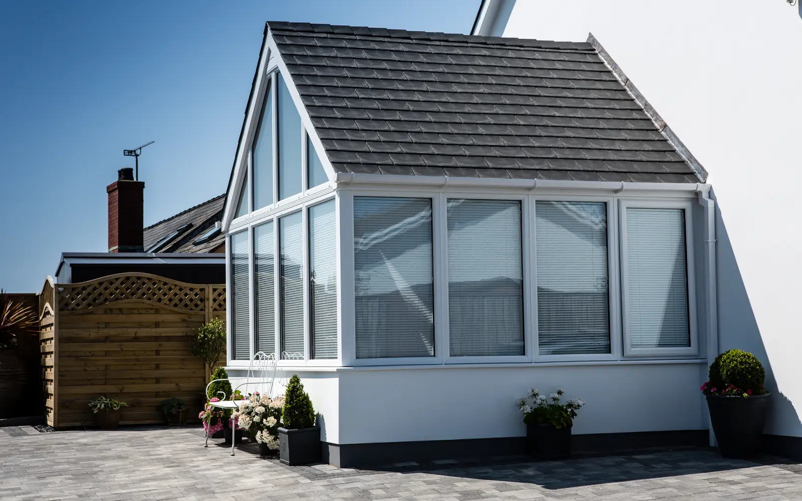 White gable-fronted conservatory with a dark tiled replacement roof